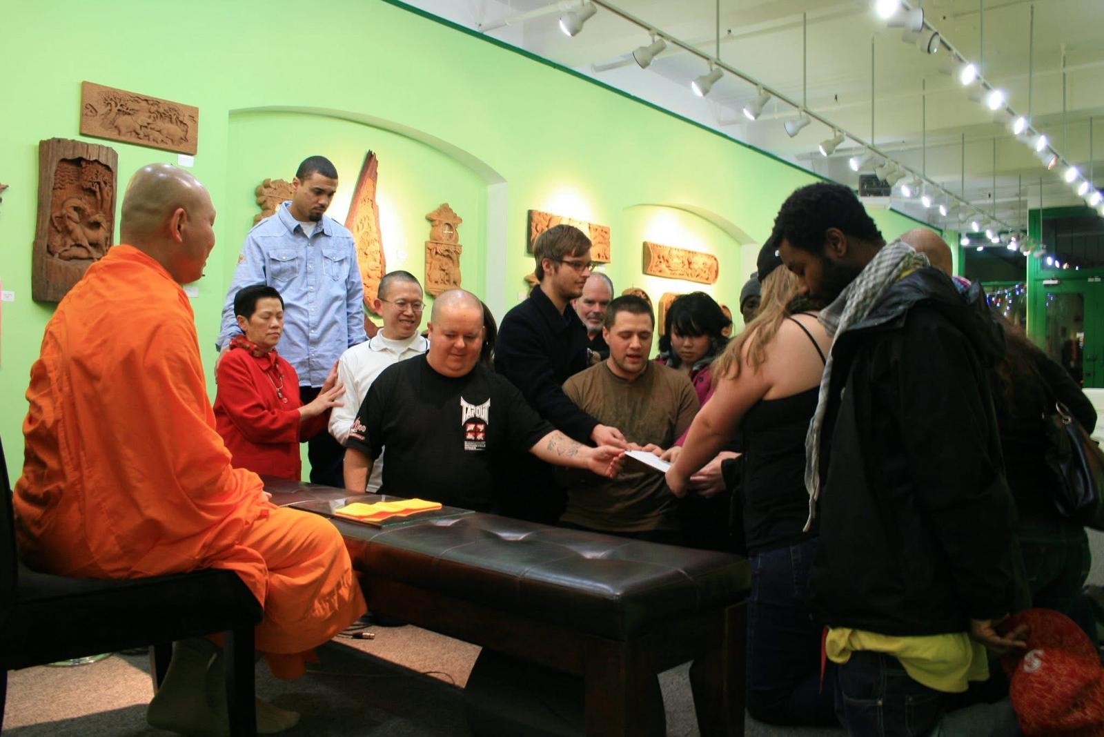 A monk talking with guests around a table in a gallery room