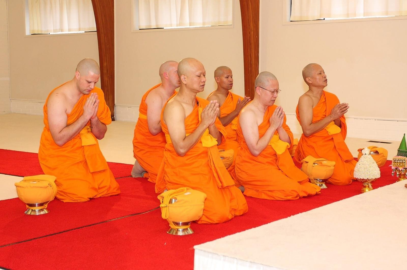 Monks kneeling with hands pressed together during a ceremony