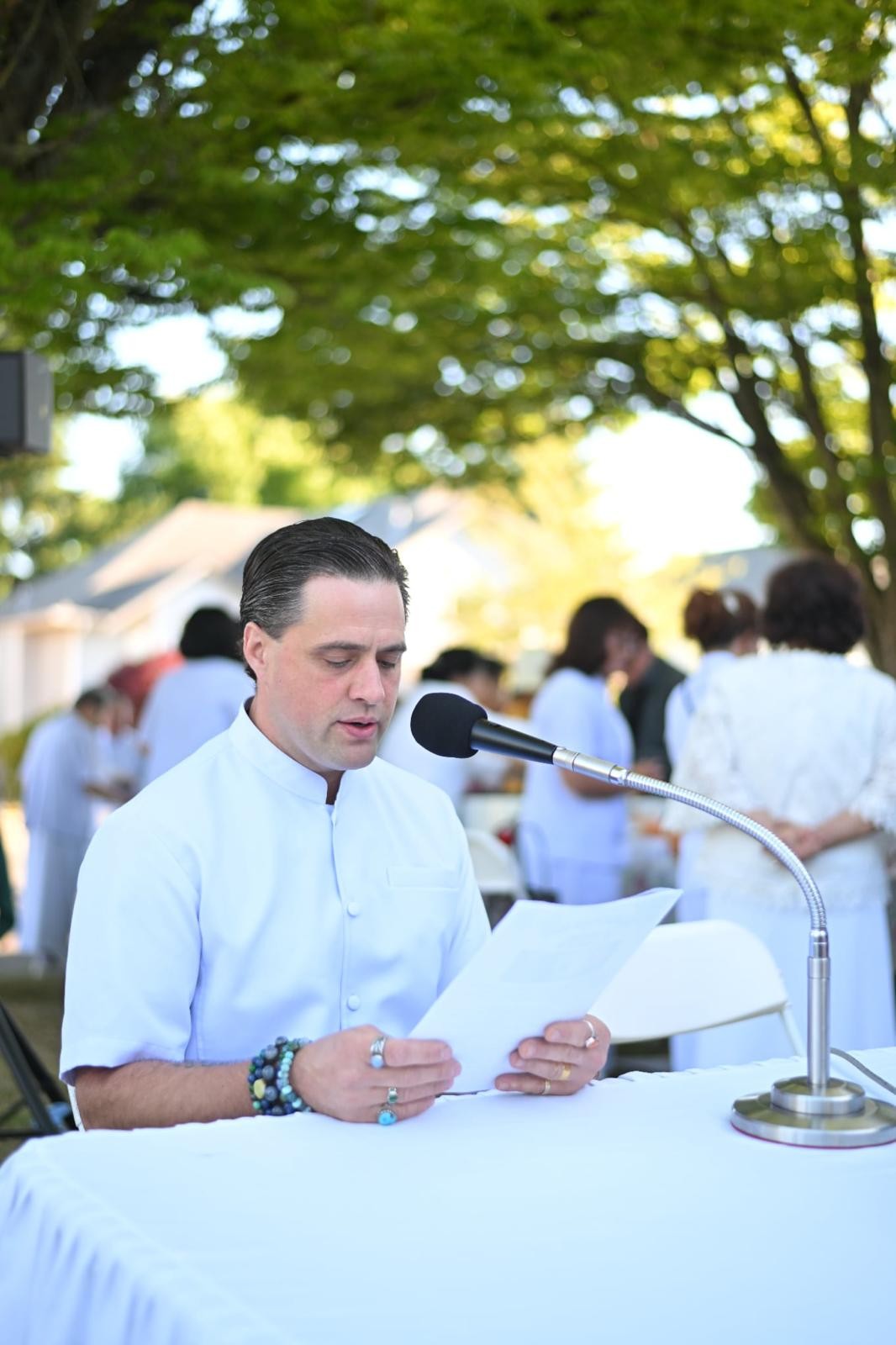Steve Pinney Jr in white reading at a microphone at an outdoor event